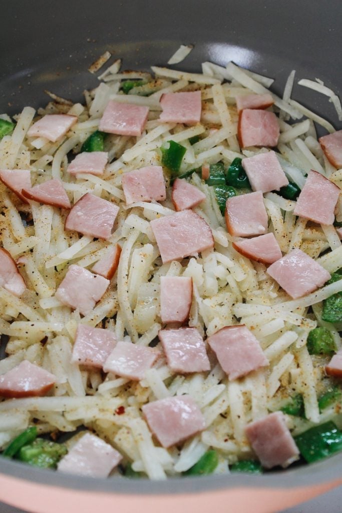 green peppers, onion, canadian bacon and hasbrowns cooking in a pan